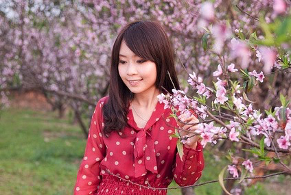 หญิงสาวในชุดสีแดงยืนข้างกิ่งดอกไม้สีชมพู