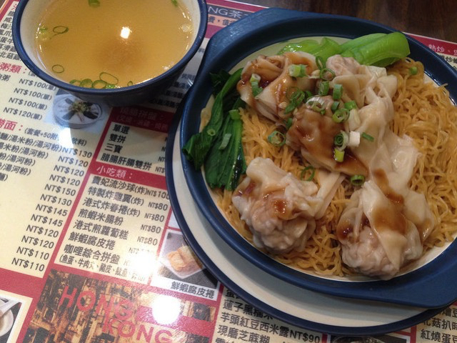 บะหมี่เกี๊ยวแห้งกับผักและถ้วยน้ำซุปวางอยู่บนเมนูร้านอาหาร